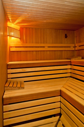 Ein leerer Sauna-Raum aus hellem Holz mit Bänken und warmem Licht.