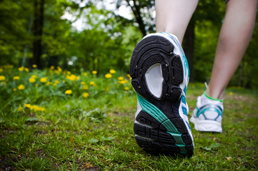 Nahaufnahme einer laufenden Person in Sportschuhen auf einem grasbewachsenen Weg mit gelben Blumen im Hintergrund.